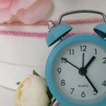 Charming blue analog alarm clock against a background of delicate flowers.