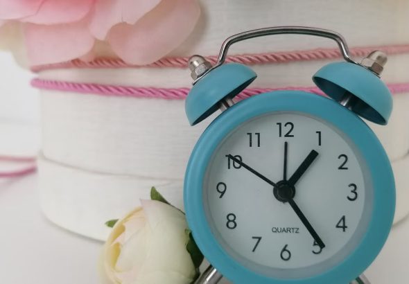 Charming blue analog alarm clock against a background of delicate flowers.