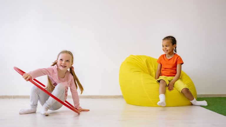 Two children enjoying playtime indoors with a hula hoop and bean bag, full of joy and fun.