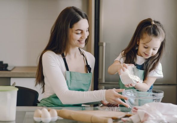 A joyful mother and daughter bonding while baking in the kitchen, smiling and enjoying the activity.